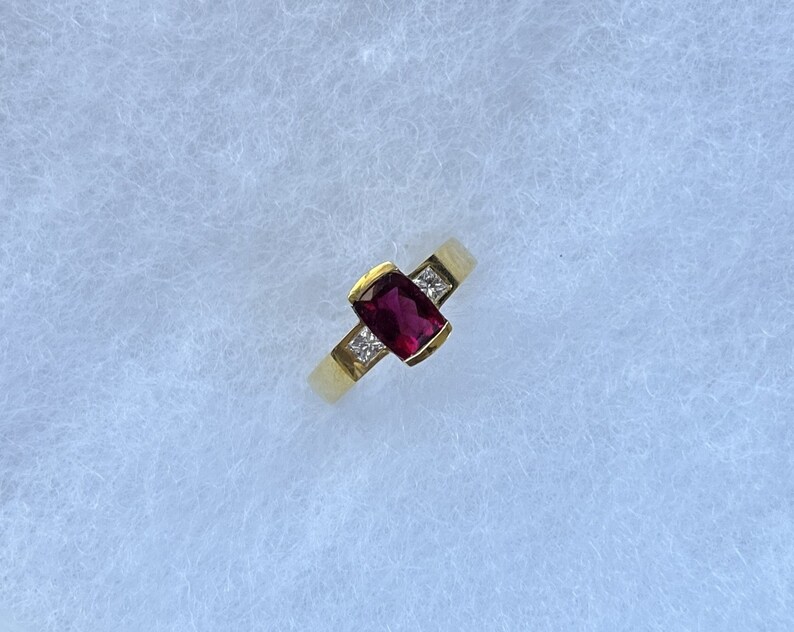 May include: A gold ring with a red gemstone and two smaller diamonds.