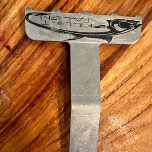 May include: A silver metal fish filleting tool with a black fish graphic and the text "Talon Fillet" on the top.