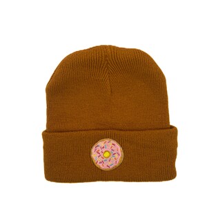 Może przedstawiać: Brązowa dzianinowa czapka z haftowanym różowym i białym pączkiem z przodu.