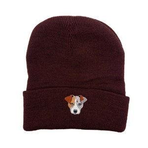 Può includere: Un berretto marrone con un cane marrone e bianco ricamato sul davanti.