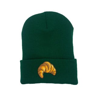 Puede incluir: Un gorro verde oscuro con un croissant bordado en amarillo y marrón en la parte delantera.