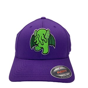 May include: Purple baseball cap with a green embroidered Cthulhu graphic. The cap has a Flexfit label with the text "The Original Flexfit L/XL It Fits Your Life".