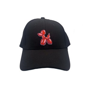 Può includere: Cappellino da baseball nero con una toppa a forma di cane di palloncino rosso e rosa.
