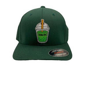 May include: A dark green baseball cap with an embroidered bubble tea design on the front. The cap has a black Flexfit label on the side.