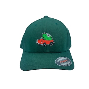May include: A green baseball cap with a frog riding in a red car embroidered on the front. The cap has a black Flexfit label on the back with the text "The Original Flexfit 110 It Fits Your Life."