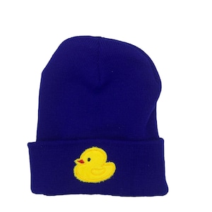 Könnte beinhalten: Eine blaue Strickmütze mit einem aufgestickten gelben Gummibärchen auf der Vorderseite.