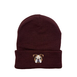 Op de afbeelding: Een donkerrode beanie met een geborduurde bruine en witte bulldog op de voorkant.