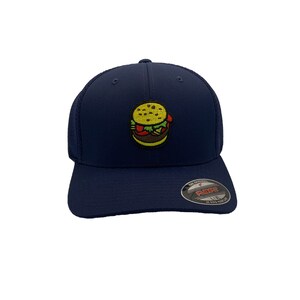 May include: A navy blue baseball cap with a mesh back. The cap features a small embroidered image of a hamburger on the front. The cap has a Flexfit label on the side.