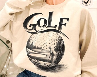 Może przedstawiać: Beżowa bluza z czarnym nadrukiem graficznym przedstawiającym piłkę golfową i golfistę. Tekst "GOLF" jest nadrukowany czarnym kolorem nad grafiką.