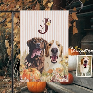 May include: A garden flag featuring two dogs with open mouths and tongues out, surrounded by pumpkins and flowers. The flag has a letter "J" with floral accents and the text "Your pet here".
