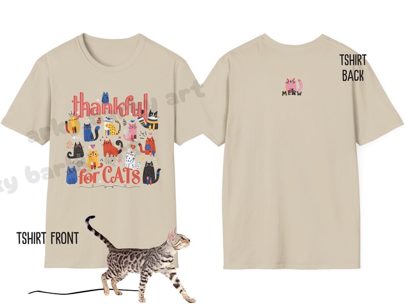 May include: Beige t-shirt with a colorful cat graphic. The front of the shirt says "thankful for CATS" in a playful font, with various cat illustrations. The back features a small pink cat and the word "MEW".