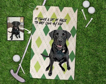 May include: A white golf towel with a green and yellow diamond pattern. The towel has the text "It takes a lot of balls to golf like my dad" printed on it. A black Labrador Retriever dog is pictured on the towel.