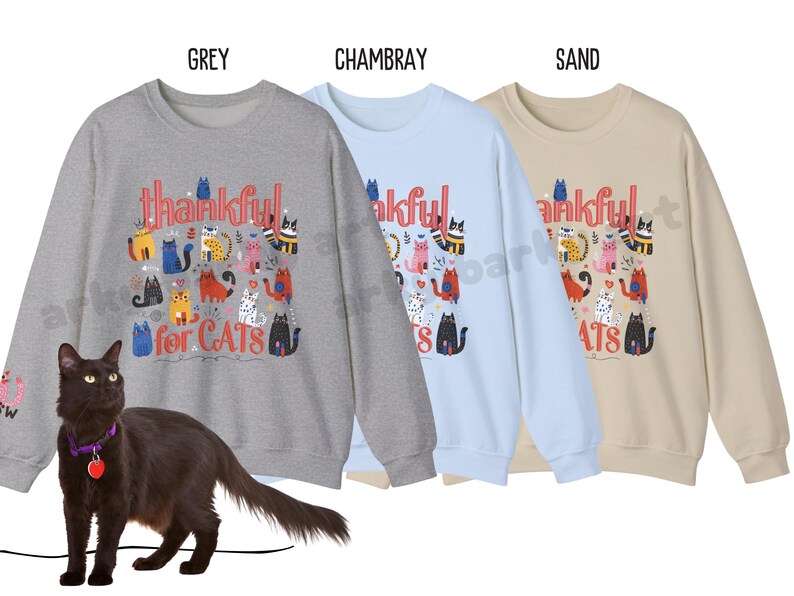 May include: Three sweatshirts in grey, chambray, and sand colors, each with a graphic of colorful cats and the text "thankful for CATS." A black cat with a purple collar and a red heart tag is in the foreground.