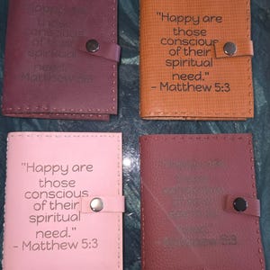 May include: Four leather journals in burgundy, tan, and pink, each with a snap closure. The journals feature the quote "Happy are those conscious of their spiritual need." from Matthew 5:3.