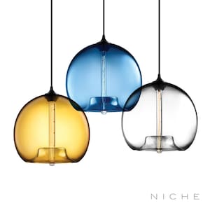 May include: Three pendant lights with spherical glass shades in amber, blue, and clear. Each light has a black cord and fixture, with a visible lightbulb inside the glass. The lights are suspended against a white background.