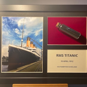 May include: Framed artwork with images of the RMS Titanic, a glass bottle, and a plaque. The Titanic is depicted at a dock. The bottle sits on a red background. The plaque reads "RMS TITANIC" and includes details.