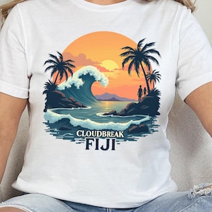 May include: White t-shirt featuring a graphic of a sunset over a beach with palm trees and a wave. The text "Cloudbreak FIJI" is printed below the graphic.