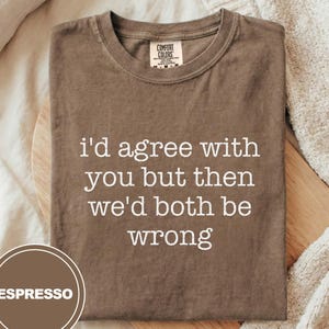 May include: Espresso-coloured t-shirt with the text "I'd agree with you but then we'd both be wrong" in white. The shirt is folded on a wooden surface, with a label that says "Comfort Colors".