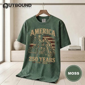 Green t-shirt with American flag, Abraham Lincoln on motorcycle, "America 250 Years" text.