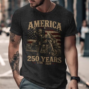 Dark t-shirt with American flag, Abraham Lincoln on motorcycle, 1776-2026 text.