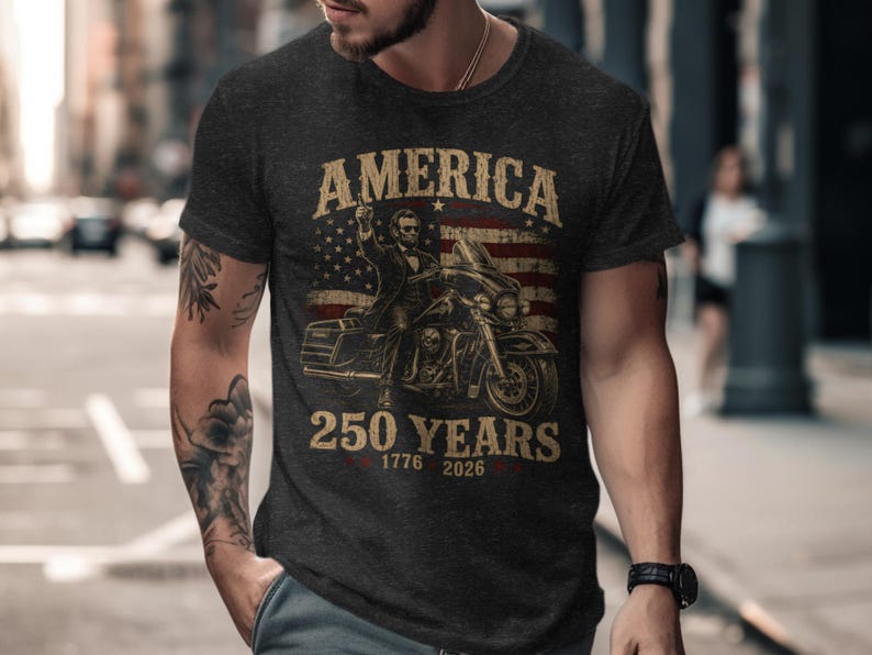 Dark t-shirt with American flag, Abraham Lincoln on motorcycle, 1776-2026 text.