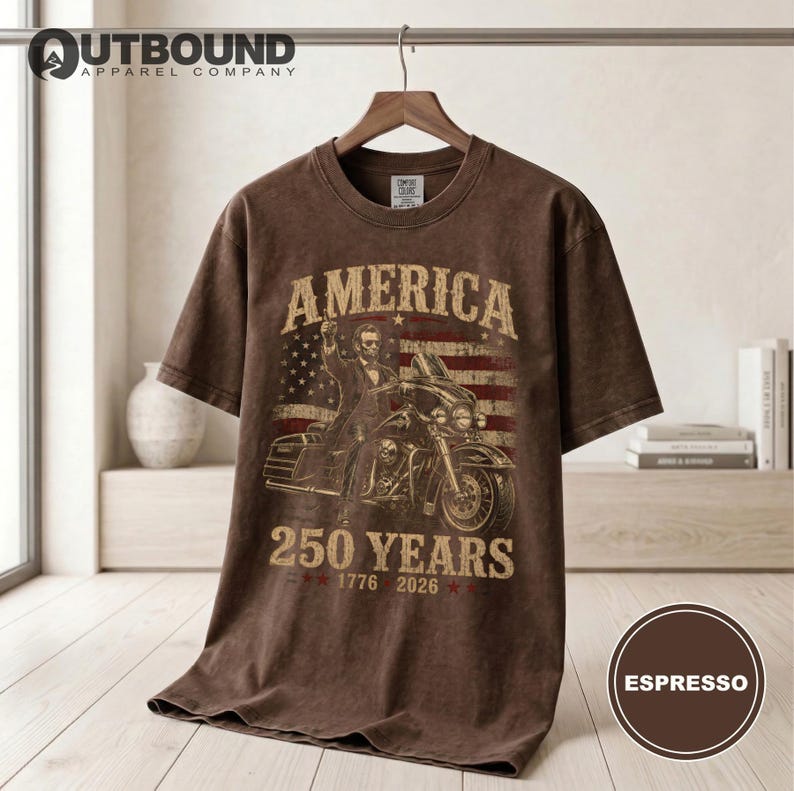 Brown t-shirt with Abraham Lincoln riding a motorcycle and American flag, "America 250 Years 1776-2026".