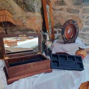 May include: A wooden jewelry box with a mirror inside and a black velvet lining. The box is open and the lid is propped up. There is a small wooden tray with compartments next to the box.