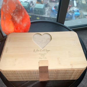May include: A light brown wooden box with a heart-shaped cutout and a brown leather strap. The box is engraved with the text "Where it all began", "Steve & Lauren", "Reading", "July 2023", and "Always & Forever".