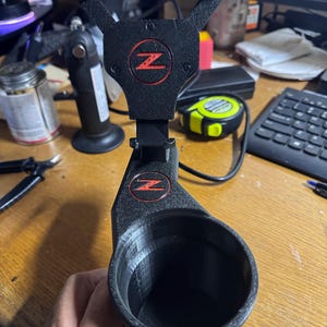 May include: A black 3D printed phone holder with a red "Z" logo. The holder has a cup holder attached to the bottom.