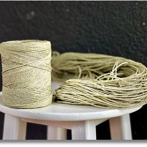 May include: Two spools of natural colored twine, one wound and one loose, on a white stool.