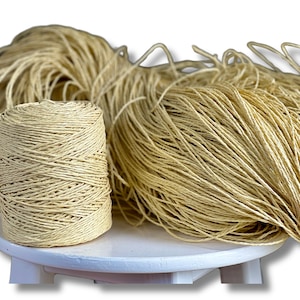May include: A spool of natural-colored twine is sitting on a white stool. The twine is made of natural fibers and is perfect for crafting, gardening, or other projects.