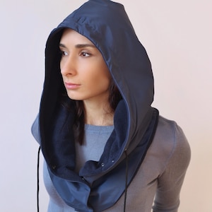 May include: A navy blue hooded neck warmer with a fleece lining. The hood is pulled up and the neck warmer is worn around the neck.