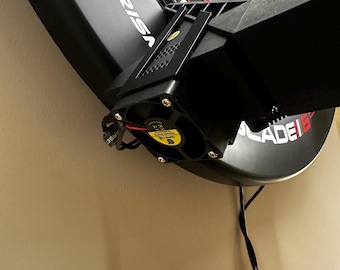 May include: Black electronic dartboard with a colorful target face. The dartboard is mounted on a wall and features the word "PRISM" and "BLADE 6" on the board. A black power cord hangs down.