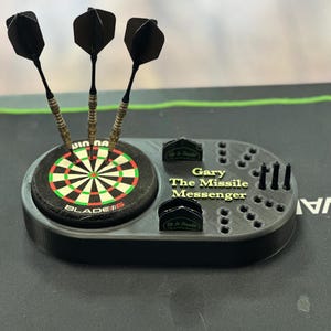 K&ouml;nnte beinhalten: Schwarzer Dart-Halter mit einem Miniatur-Dartboard, drei Darts und dem Text "Gary The Missile Messenger". Der Halter hat Schlitze f&uuml;r Darts und Zubeh&ouml;r. Der Text "Up In Smoke" ist ebenfalls sichtbar.