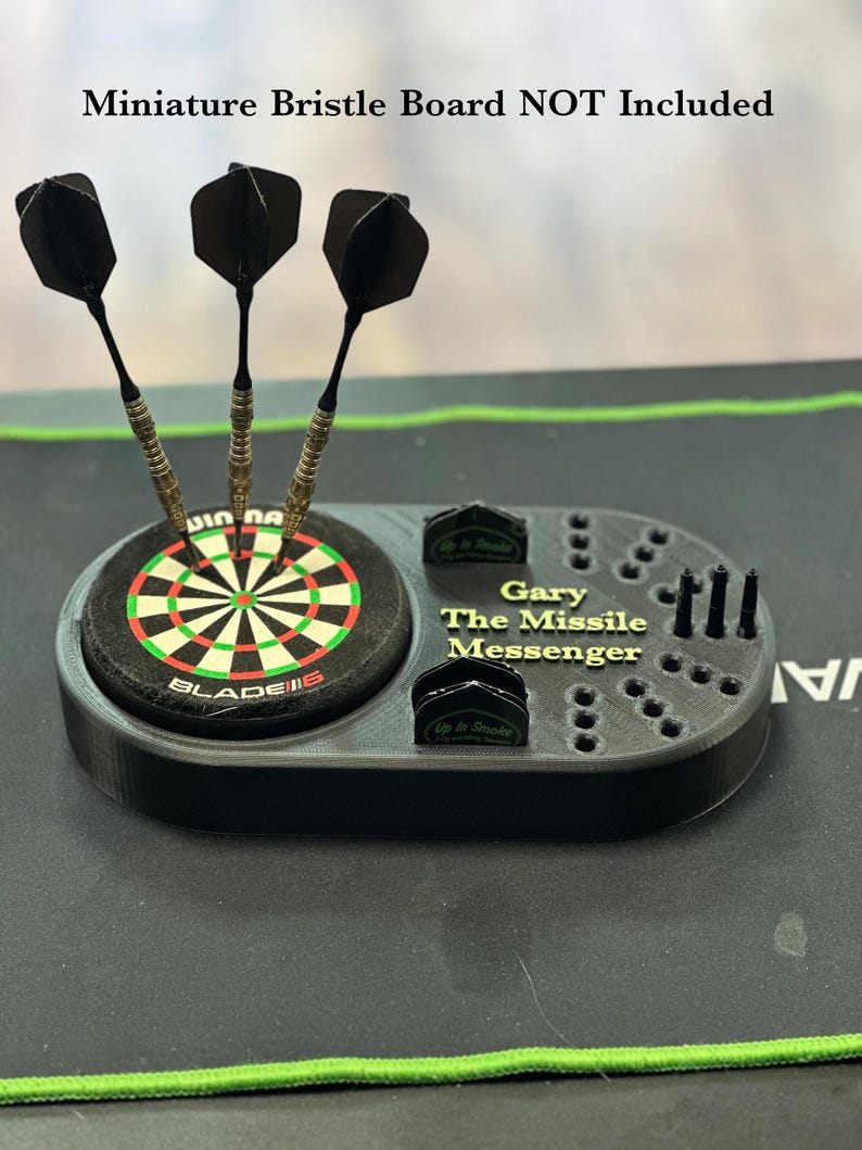 K&ouml;nnte beinhalten: Schwarzer Dart-Halter mit einem Miniatur-Dartboard, drei Darts und dem Text "Gary The Missile Messenger". Der Halter hat Schlitze f&uuml;r Darts und Zubeh&ouml;r. Der Text "Up In Smoke" ist ebenfalls sichtbar.