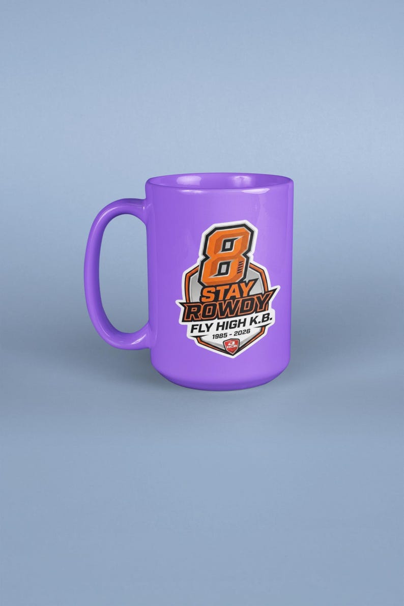 May include: A purple ceramic mug featuring a graphic design with a large orange number 8, the text STAY ROWDY, FLY HIGH K.B., and the years 1985-2026. The design is enclosed in a shield-shaped emblem with black, white, and orange accents.