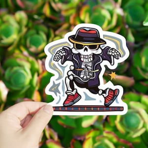 May include: A cartoon skeleton wearing a black and white hat, sunglasses, and a black jacket with a white skeleton design. The skeleton is dancing on a red and black checkered platform.