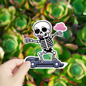 May include: A cartoon skeleton wearing a black shirt and shorts is riding a skateboard. The skeleton has a pink cloud above its head and is sticking its tongue out.