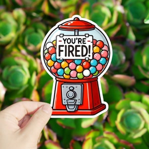 May include: A red gumball machine with a sign that reads "You're Fired!" The machine is filled with colorful gumballs.