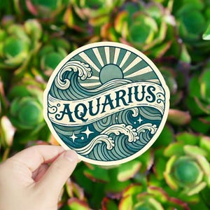 May include: A round sticker with a vintage design featuring a sun, waves, and stars. The text "AQUARIUS" is written in a banner across the waves.