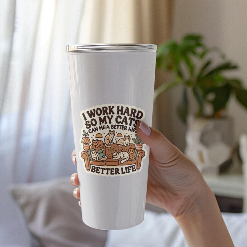 May include: White tumbler with a sticker that says "I work hard so my cats can have a better life." The sticker features a cartoon illustration of cats sitting on a couch.
