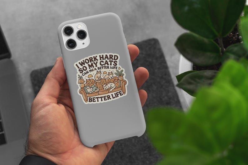 May include: A white phone case with a colorful illustration of cats sitting on a couch. The text on the case reads "I work hard so my cats can have a better life".