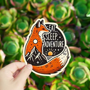 May include: A sticker featuring a cartoon fox with a mountain and sunset scene inside its body. The text "Eat, Sleep, Adventure" is written on the sticker.