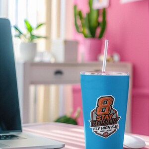 May include: A bright blue stainless steel tumbler with a clear lid and a white straw. The front features a graphic with a large orange number 8, the text STAY ROWDY, FLY HIGH K.B., and the years 1985-2026 inside a shield-shaped emblem.