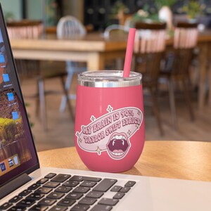 May include: A pink insulated wine tumbler with a silver rim and a pink straw. The tumbler has a sticker that reads "My Brain is 90% Taylor Swift Lyrics" with an open mouth graphic.