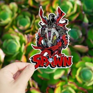 May include: A red, black, and white sticker featuring a comic book character with a skull on his chest and the word "SPAWN" in large red letters.