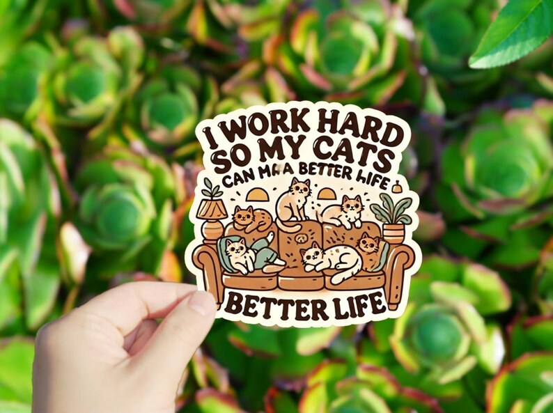 May include: A sticker with a cartoon illustration of cats sitting on a couch. The text reads "I work hard so my cats can have a better life" and "Better Life".