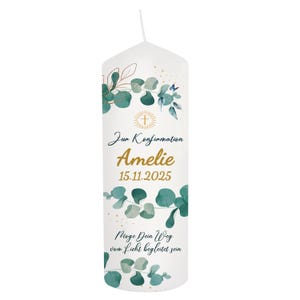 May include: White candle with green eucalyptus leaves and gold accents. The candle has text in German, including the name "Amelie" and the date "15.11.2025". A gold cross is also featured.