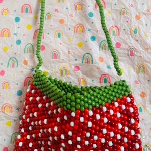 May include: A red and white beaded strawberry-shaped purse with a green beaded strap.