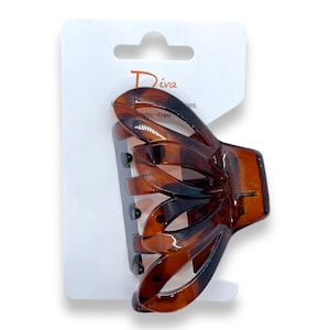 Puede incluir: Una pinza para el pelo de plástico marrón con un diseño decorativo e intrincado. La pinza está en una tarjeta blanca con la palabra "Diva" impresa en ella.